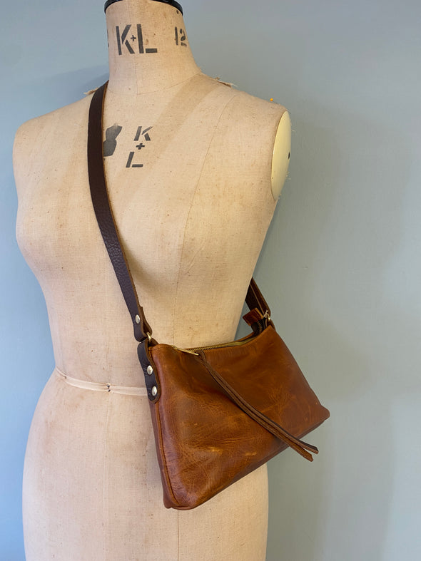 Small brown leather bag on a mannequin torso against a plain background