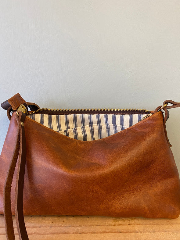 Brown leather handbag with striped lining on a wooden surface