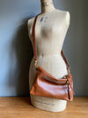 Crossbody handbag in tan brown leather with zipped exterior pocket and adjustable crossbody strap by Ginger and Brown shown on a vintage tailor's dummy. 