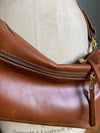 Close up of a crossbody handbag in tan brown leather with zipped exterior pocket and adjustable crossbody strap by Ginger and Brown shown on a vintage tailor's dummy. 