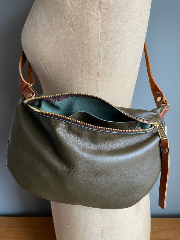 Dark olive half moon bag in leather, a passport/travel bag shown on a vintage dressmakers dummy