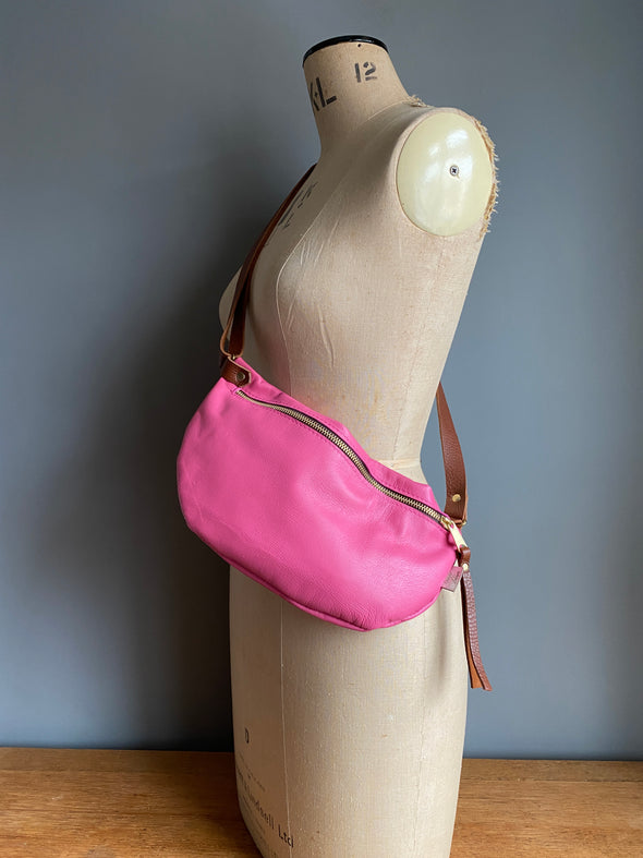 A pink leather half moon crossbody bag shown on an antique tailors dummy