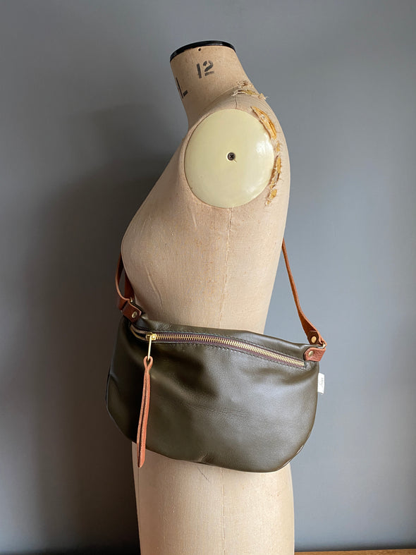 Dark olive half moon bag in leather, a passport/travel bag shown on a vintage dressmakers dummy