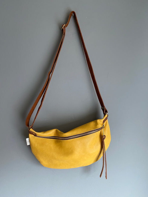 A leather crossbody travel bag with a leather strap hanging on a wall hook 