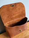 Tan brown leather handbag with crossbody strap shown with flap open to view the inner pocket