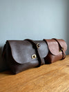 A side view of two leather handbags in dark brown and a tan brown with crossbody straps