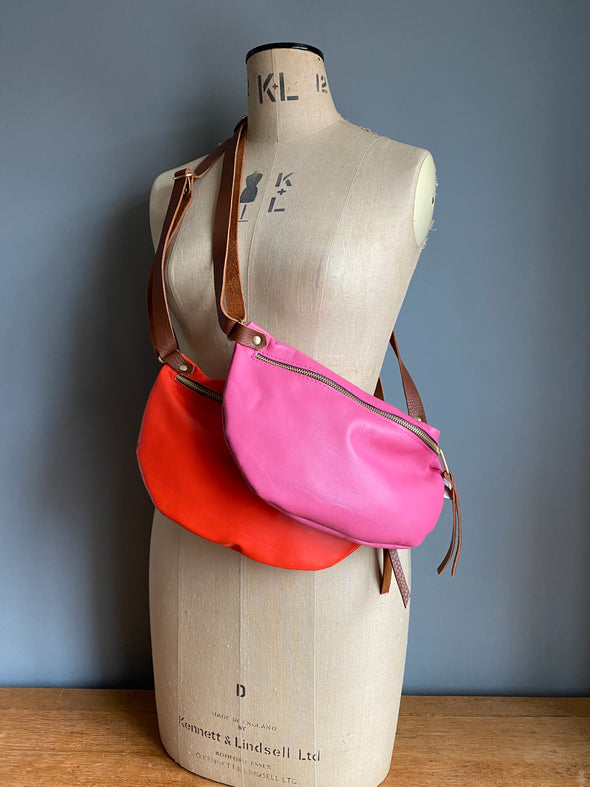 A tomato red and pink leather half moon crossbody travel bag worn by an antique tailors dummy