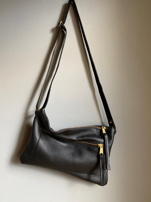 Crossbody handbag in black leather with zipped exterior pocket and adjustable crossbody strap by Ginger and Brown. 