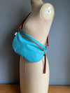 A turquoise blue leather half moon crossbody bag worn by an antique tailors dummy