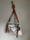 Crossbody handbag in silver leather with zipped exterior pocket and contrasting brown strap by Ginger and Brown shown hanging on a hook.