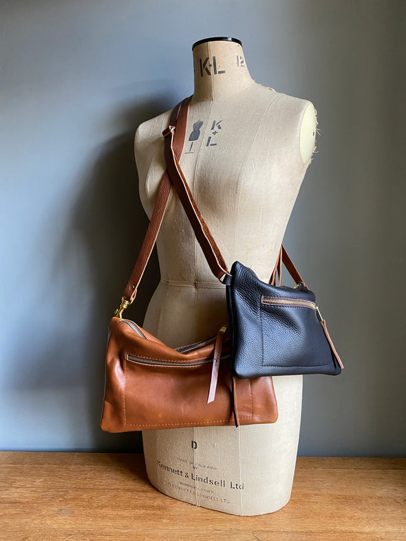 Crossbody handbag in tan brown leather with zipped exterior pocket and adjustable crossbody strap by Ginger and Brown shown on a vintage tailor's dummy. 