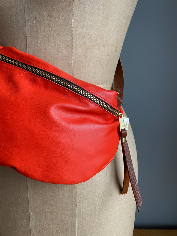 A tomato red leather half moon crossbody bag worn by an antique tailors dummy