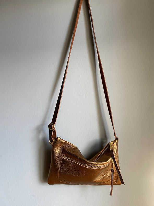 Bronze leather crossbody handbag with zipped exterior pocket and contrasting dark brown strap by Ginger and Brown shown hanging on a wall hook.