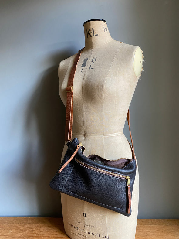 Crossbody handbag in dark brown leather with zipped exterior pocket and contrasting brown strap by Ginger and Brown shown on a vintage tailor's dummy. 