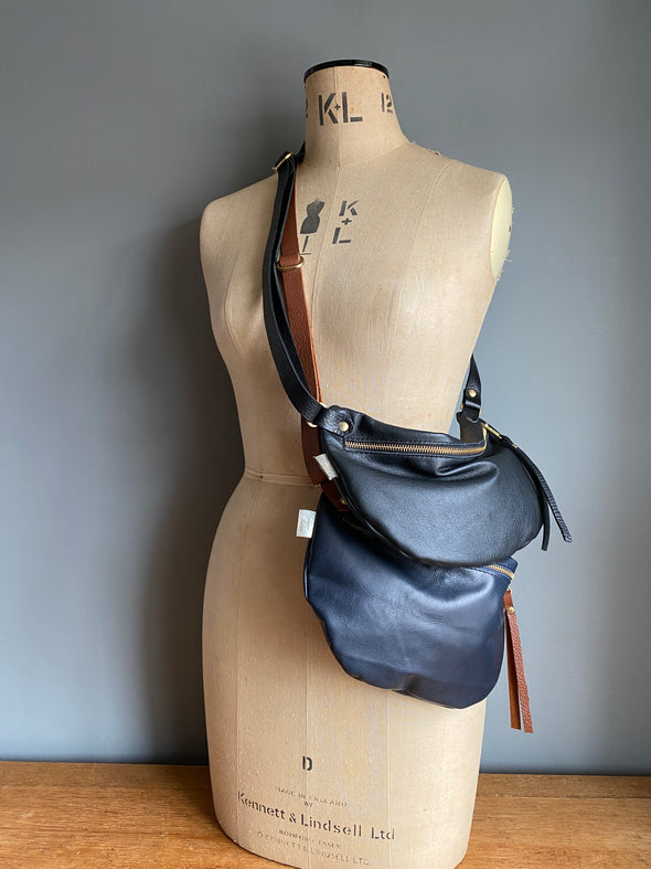 Two half moon bags in leather,  a black and a dark blue passport/travel bag shown on a vintage dressmakers dummy