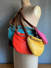 A collection of colourful red, turquoise, pink and yellow half moon travel bags  shown on a vintage tailors dummy