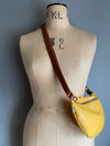 A yellow leather half moon crossbody bag worn by an antique tailors dummy