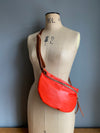 A tomato red leather half moon crossbody bag worn by an antique tailors dummy