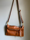 Crossbody handbag in tan brown leather with zipped exterior pocket and adjustable crossbody strap by Ginger and Brown .