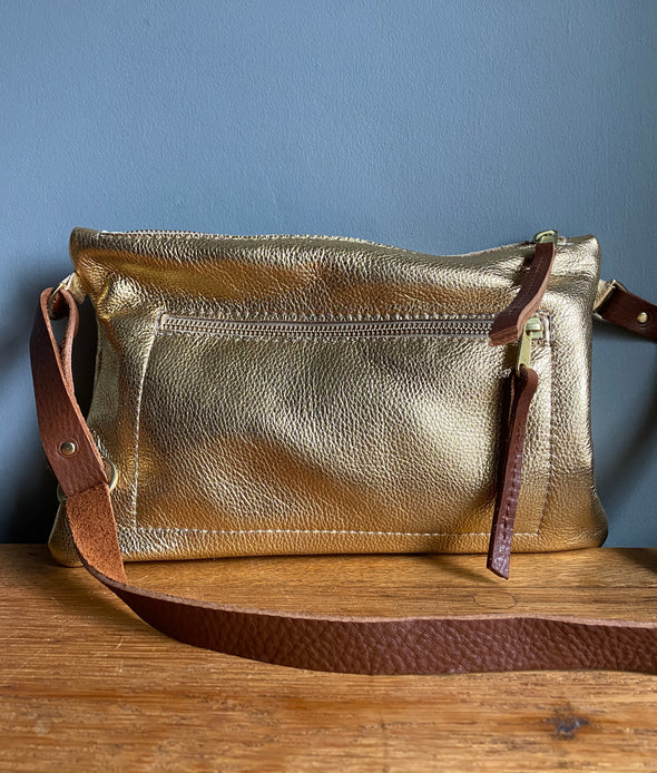 Gold leather crossbody handbag with zipped exterior pocket by Ginger and Brown shown on a wooden table. 