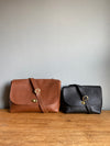 black leather crossbody handbag and a brown leather purse on a wooden table