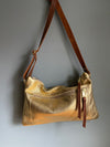 Gold leather crossbody handbag with zipped exterior pocket by Ginger and Brown shown hanging from a hook. 