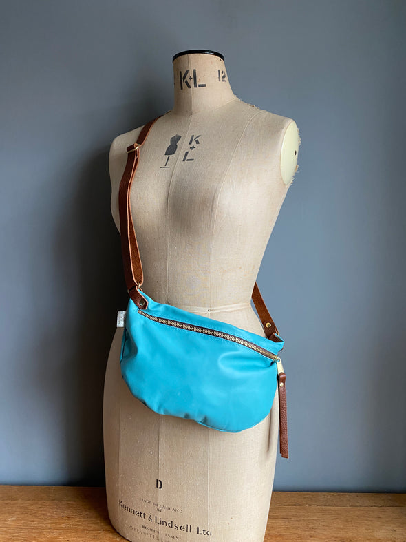 A turquoise blue leather travel crossbody bag shown on an antique tailors dummy