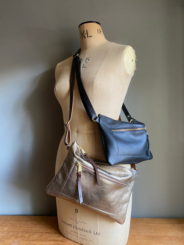 Crossbody handbag in black leather with zipped exterior pocket and adjustable crossbody strap by Ginger and Brown shown on a vintage tailor's dummy. 