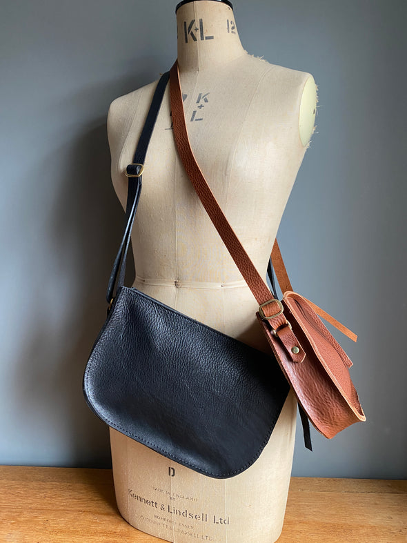 Two crossbody leather purses shown on a vintage tailor's dummy