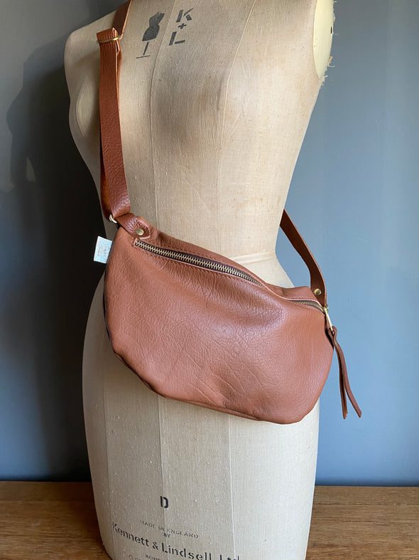 Tan brown half moon bag in leather, a butterscotch brown passport/travel bag shown on a vintage dressmakers dummy