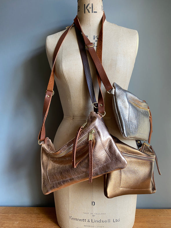 A collection of metallic leather crossbody handbags with zipped exterior pocket and contrasting brown strap by Ginger and Brown shown on a vintage tailors dummy.