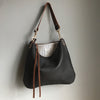 Dark brown leather purse with a shoulder strap shown hanging on a wall hook