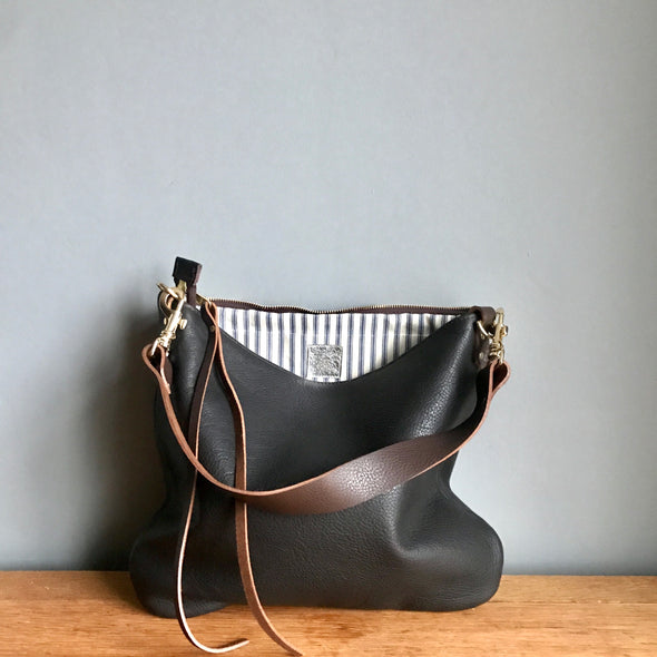 Dark brown leather handbag with a shoulder strap shown on a wooden table