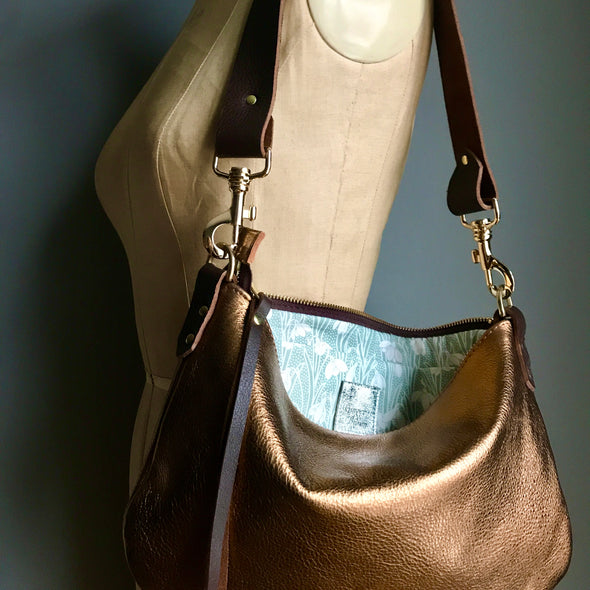 Bronze leather purse with shoulder strap shown on a vintage tailor's dummy